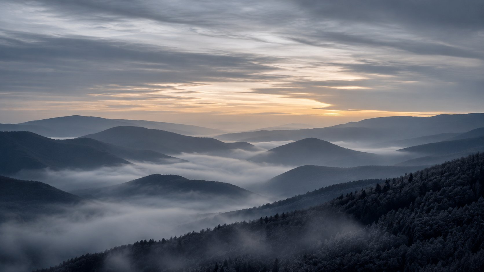 Misty mountain valleys at sunrise with layered forested peaks and low-lying clouds