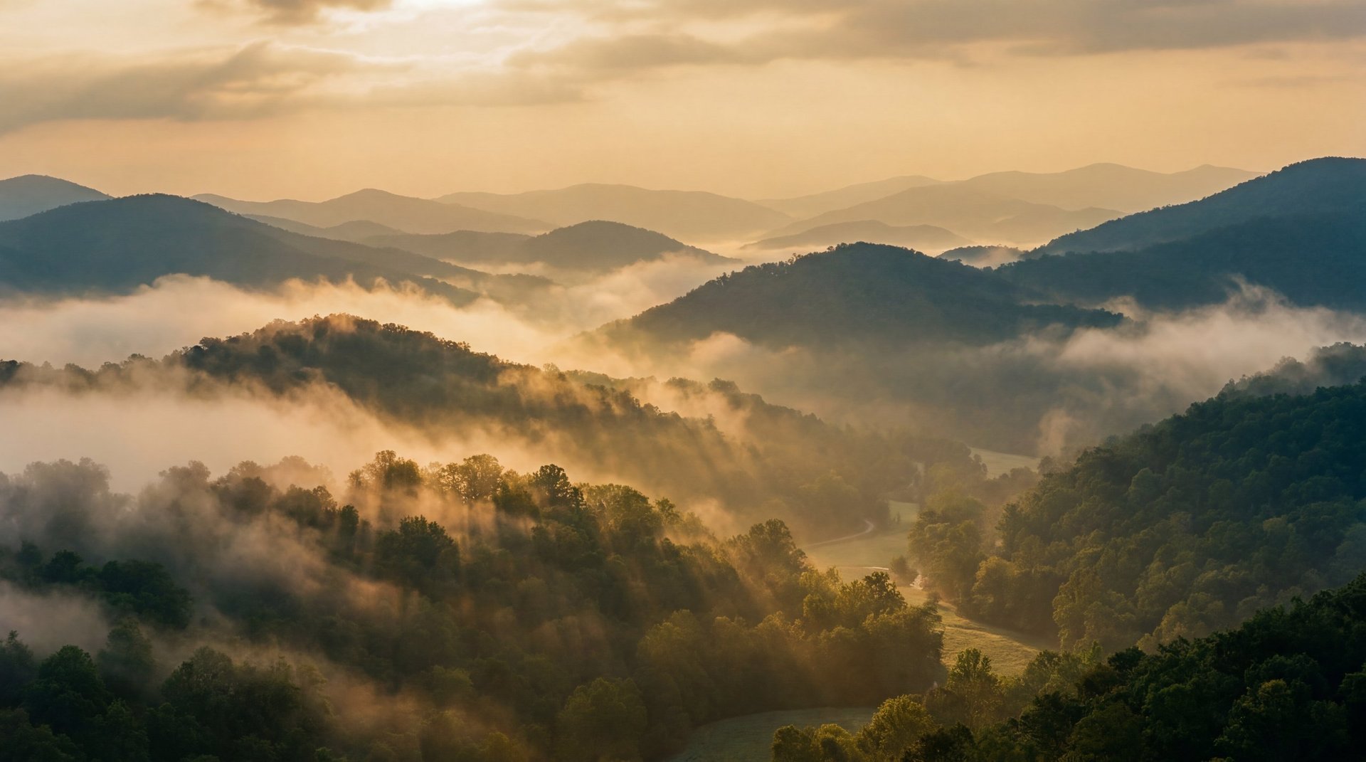 Misty mountain valley at sunrise with layers of forested hills and golden light breaking through fog